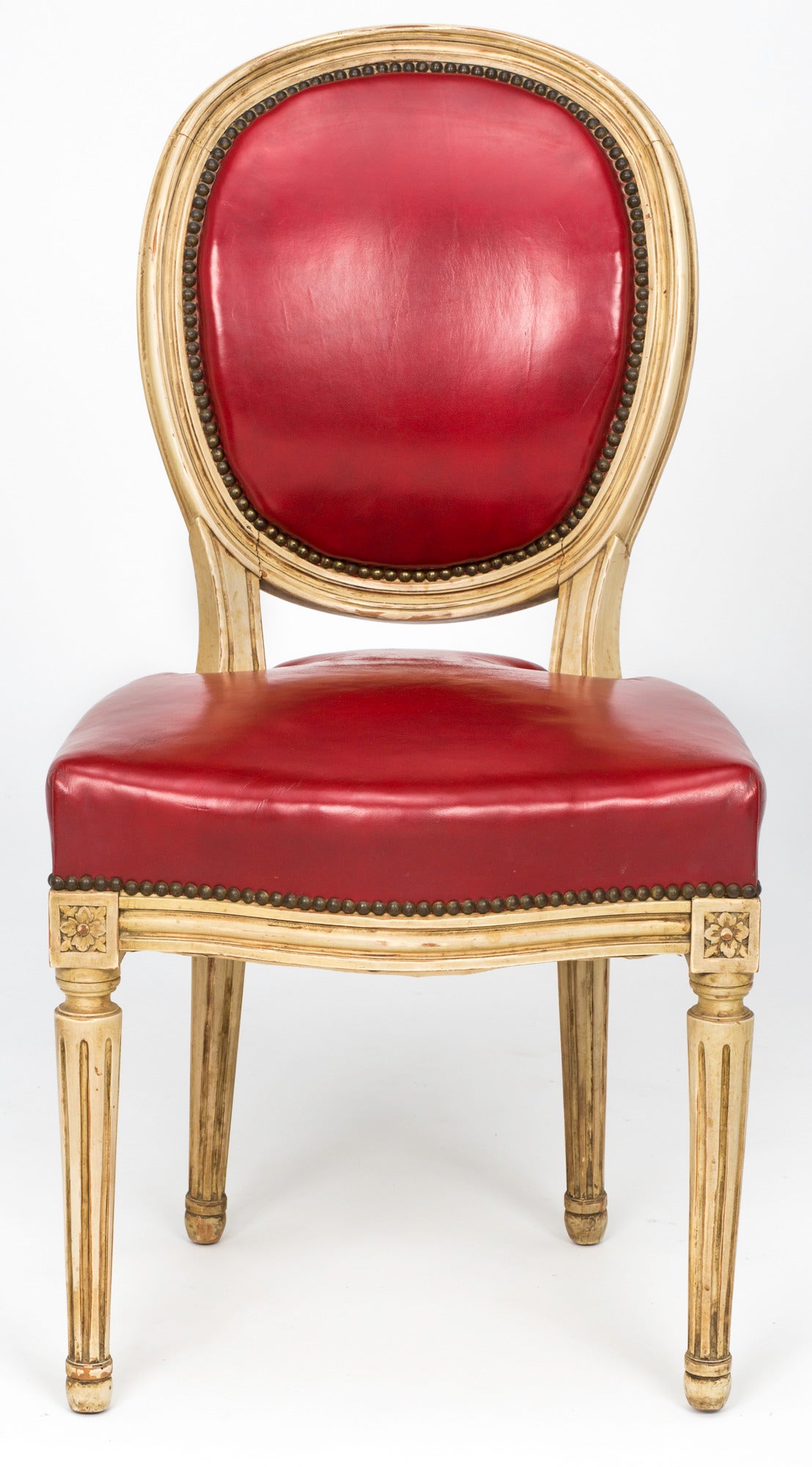 Pair of French Louis XVI style chairs in antique cream painted finish. Frames are from 1880s. Later upholstered in clean bright red leather. Finished with decorative brass nail studs. Great accent chairs or desk chair.