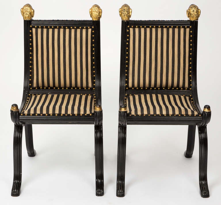 1930s Italian. Decorative accent chairs with gilt carved ram's heads. Ebonized grooved wood frame, upholstered in woven cream and black stripe fabric. Accent trim with antique brass studs.