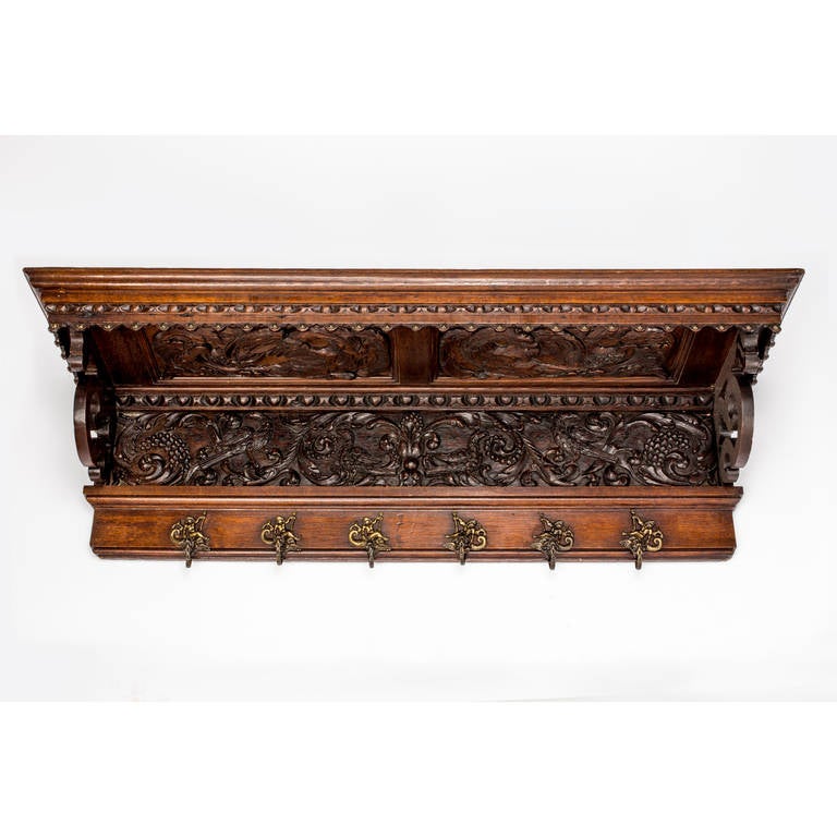 19th Century Beautiful and intricately carved coat or hat rack in dark English oak. Elaborate carved panels are above the rack as well as  on the front. There are six brass hooks in Neptune-like figures.
Very decorative and functional piece.
