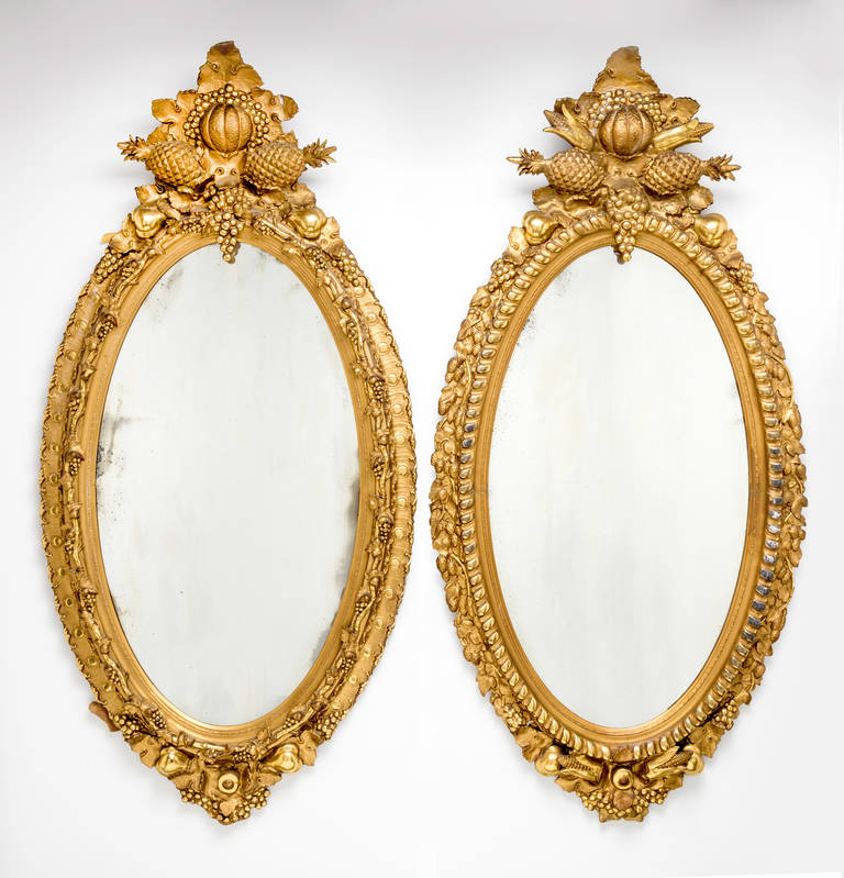 Fabulously dramatic wood carved oval gilt frame mirrors.  Crowned with abundant horn of plenty fruit motif. Spectacular mirrors from 1870s. Not identical but close enough if used as a pair. Hard to find a pair.
Priced and sold individually.