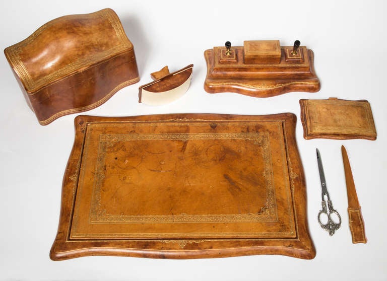 Beautifully  aged, warm caramel color leather set tooled in gold.  The extensive set includes reversible writing pad, large letter holder, note pad, pen cradle, blotter and letter opener  with scissors.  All very beautiful.  Back of the writing pad