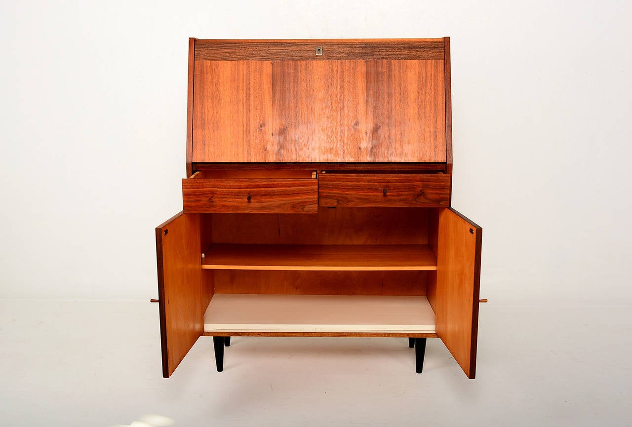 For your consideration a mid century secretary desk constructed with walnut plywood, mounted in four peg legs in black. 

Drop down desk with open storage. 
Features two pull out drawers and open storage with single shelf.

Doors open and close
