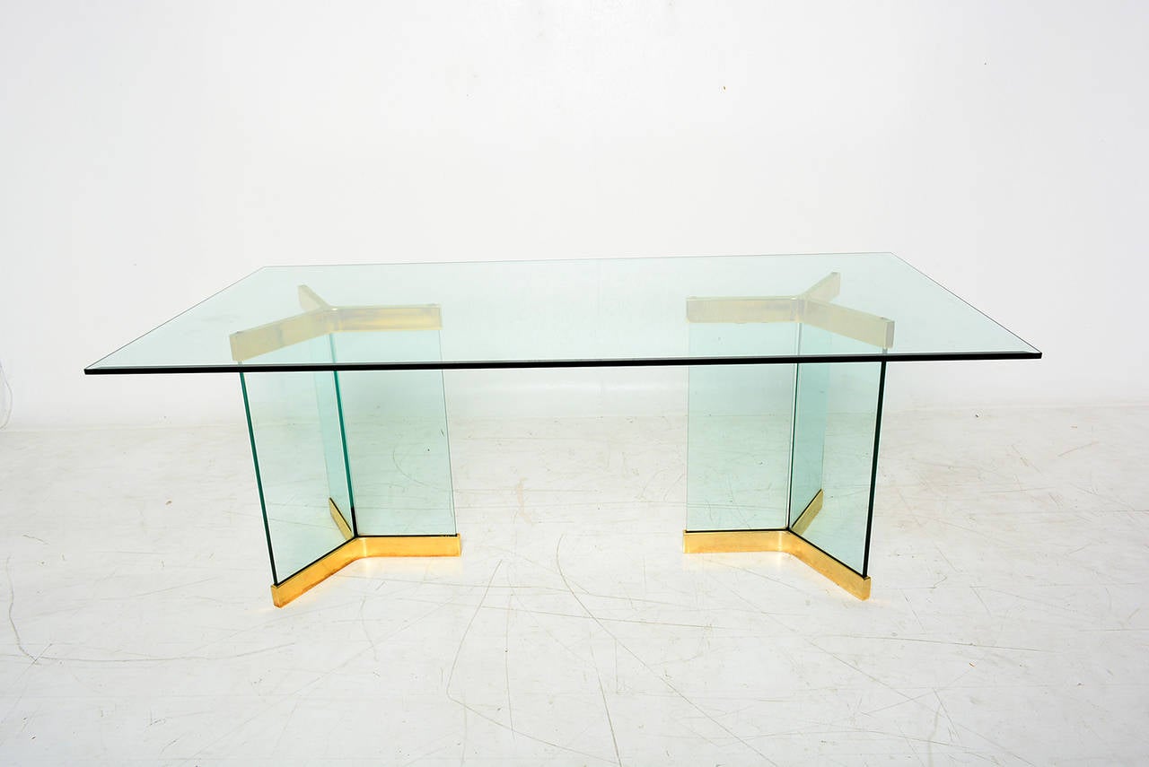 For your consideration a vintage dining table. Glass top with beveled edged.

Bases if formed with two pedestals of glass connected by a triangular frame of brass-plated steel. Unmarked. 

Seat six.