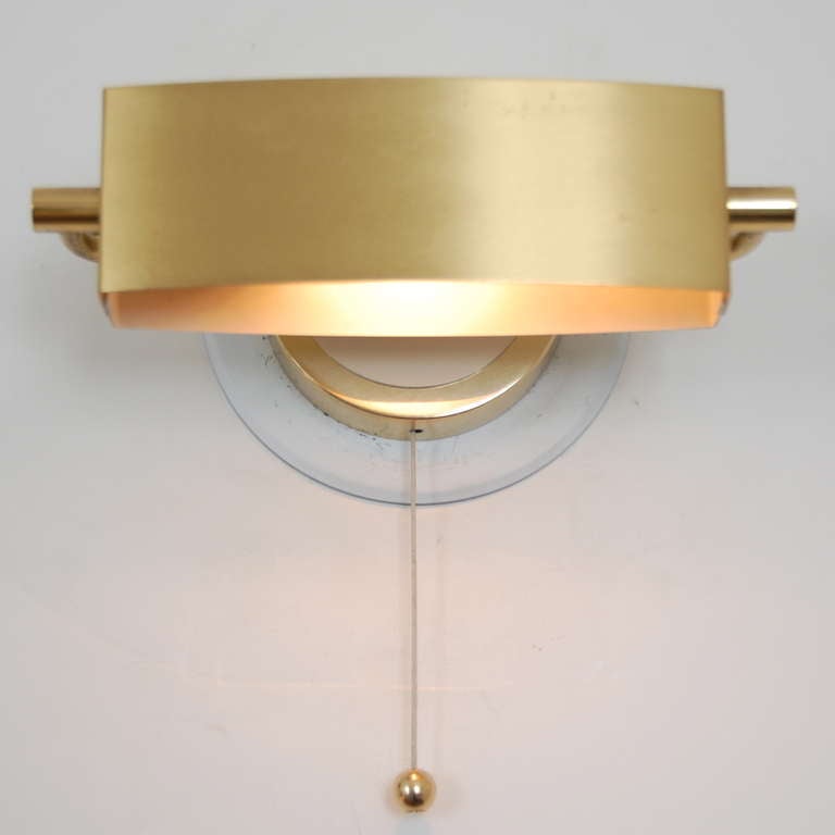 Two discreet brass wall sconces by Jacques Biny. These sconces, with directional shades and pull switch, are ideal for reading and subtle lighting accent.  