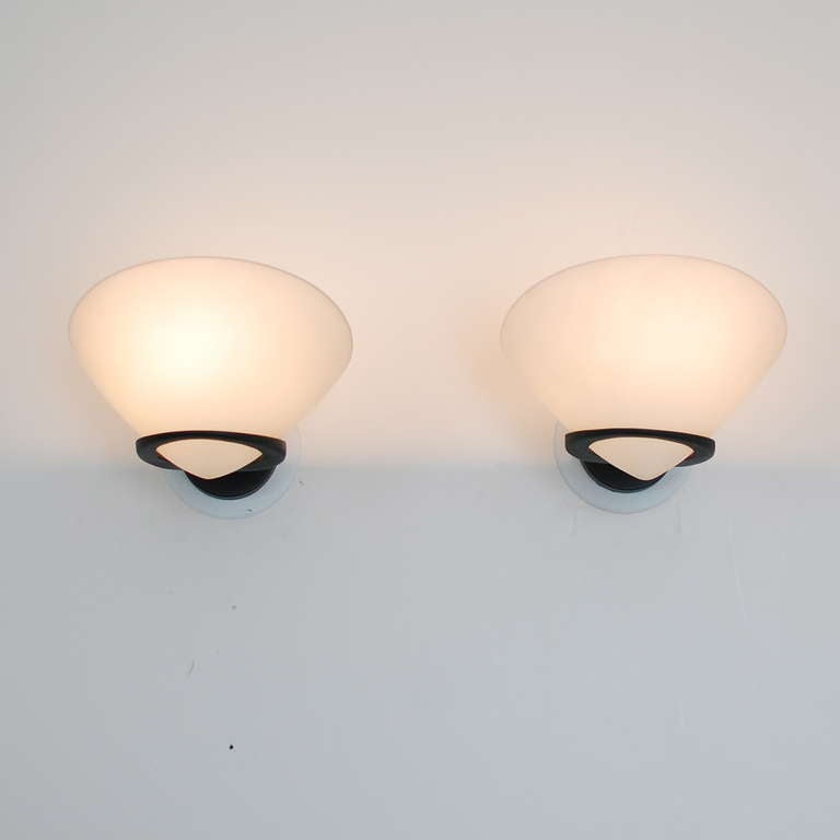 Two pairs of Italian sconces. They have a beautiful minimal bracket design, which holds a delicate white satin blown glass shade. These sconces give indirect as well as direct light emanating from a single lightbulb. 
Black back plate is 3.5