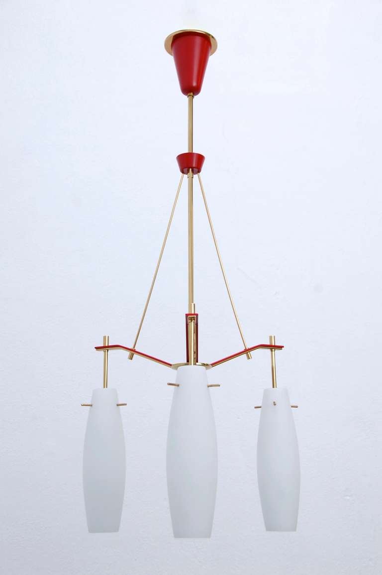3 Glass shade chandelier attributed to Stilnovo, circa 1958, possessing a fine brass finish combined with a red accent. This chandelier is both delicate and tense due to combining a structural design with glass. 

Diameter: 22