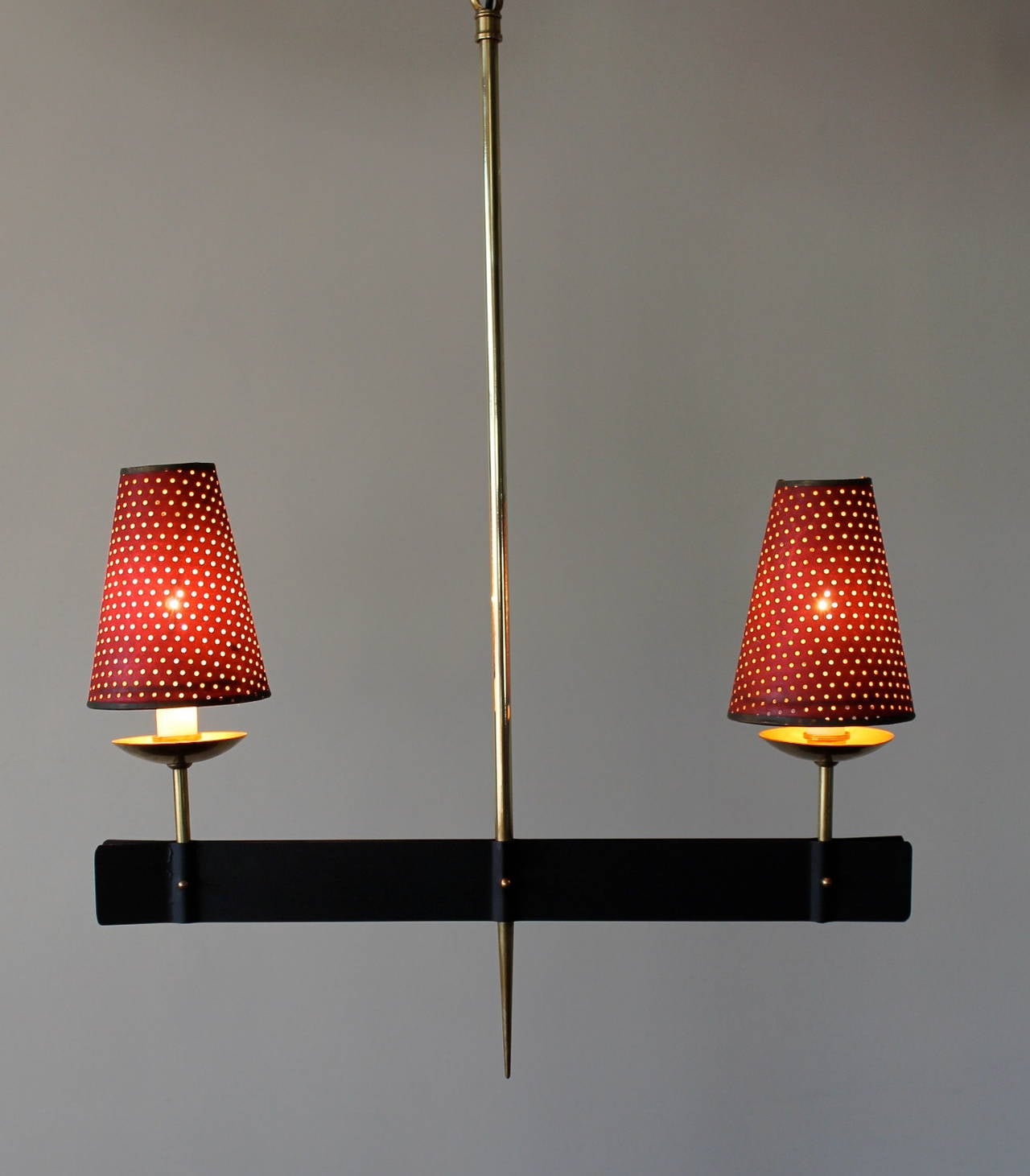 Hanging French lamp made of brass and iron with two lights covered with petite perforated paper shades in a vintage burgundy color. A solid brass slender spear in middle with an iron bar crossing over on the bottom holding a lamp on each side.