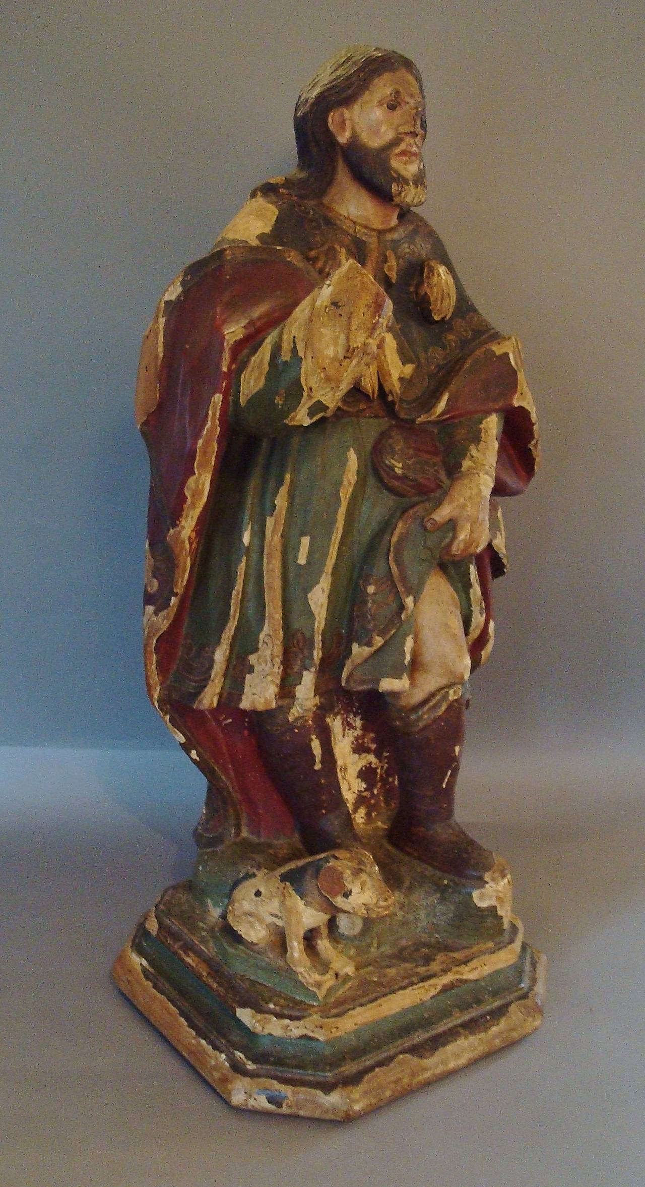 18th century carved and polychrome statue of Saint Roch, dressed in a colorful, long flowing cloak, with carved shells, his right arm aloft (missing hand), his left hand lifting his robe to show his leg, his seated dog at his side, the reverse