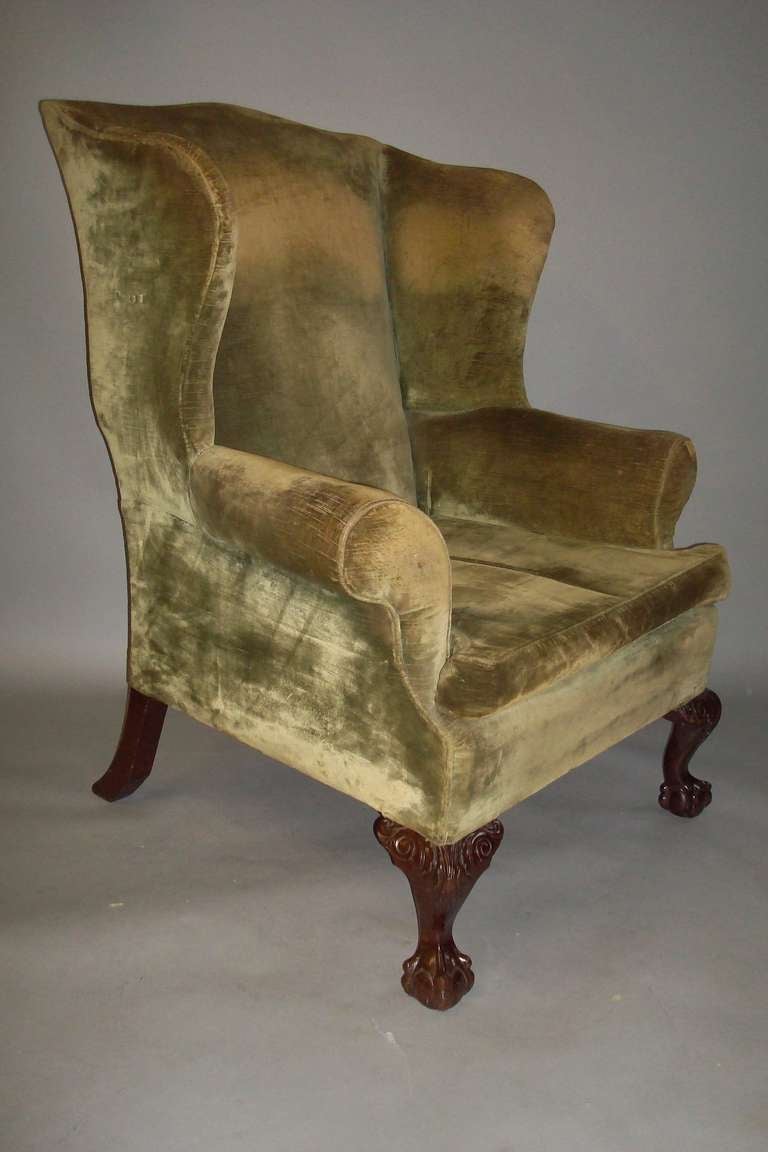 A 19th century wing chair of large proportions in the Georgian style, the well shaped back and wings leading to a padded scroll arms; with a squab cushion seat, upholstered in old sage green velvet, raised on front cabriole legs with acanthus