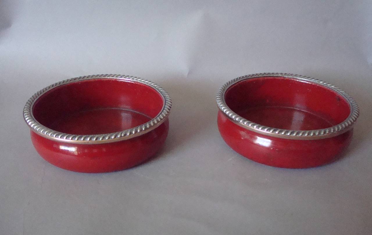 A fine English Regency pair of papier mâché wine coasters, of large proportions, the Sheffield silver plated rims with gadrooning and beaded decoration, above the moulded shaped body in scarlet japanned papier mache.  The underside with baize