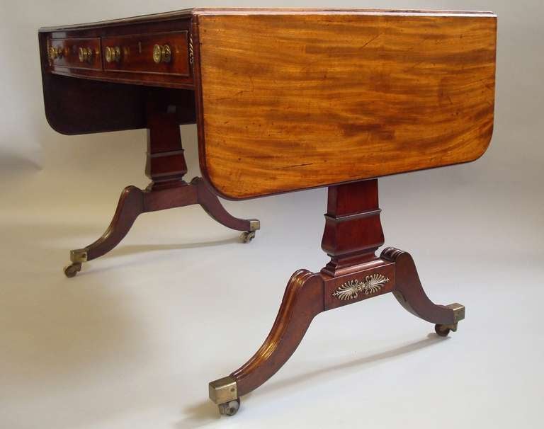 A good Regency mahogany and brass-mounted sofa table, the well figured rectangular top with rounded corners to the flaps all with a moulded edge, above two frieze drawers with cock beaded edges and brass knob handles; incorporating mahogany drawer