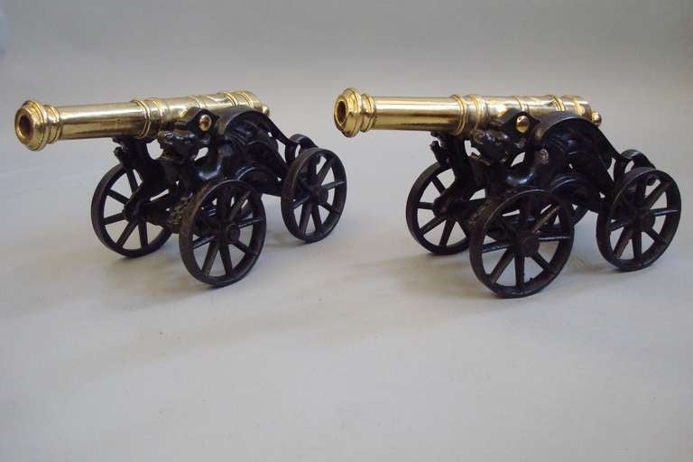 C19th pair of ornamental brass cannons on cast iron 4 wheel carriages; the tilting brass barrels raised on a twin pierced griffin supports, with open mouths, shaped wings and scrolling tails, all standing on four, 8-spoke turning carriage wheels.