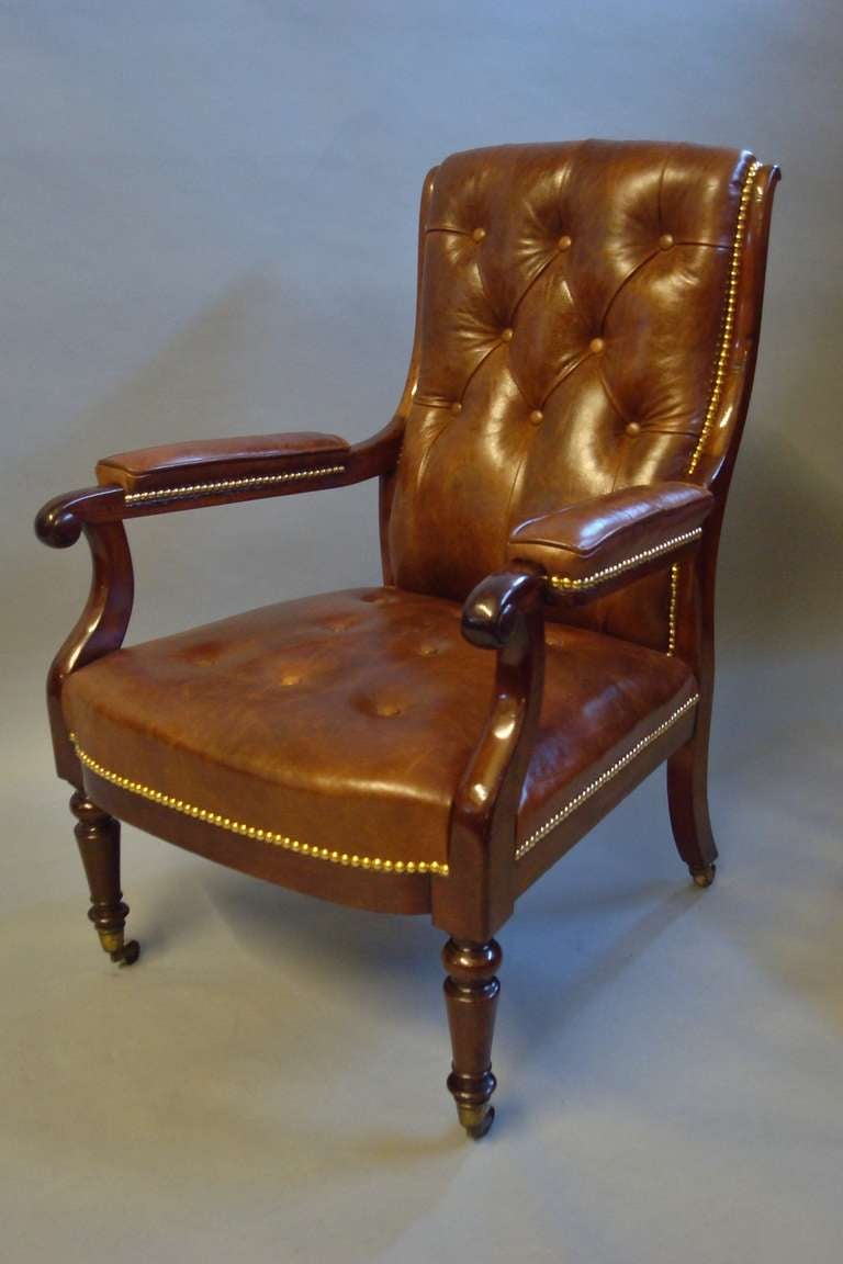 A good Regency mahogany and leather library open armchair; the shaped padded back with deep buttoning; the scrolled side supports leading to padded arm rests with piped edges; the shapely arm supports with turned roundels leading to a padded and