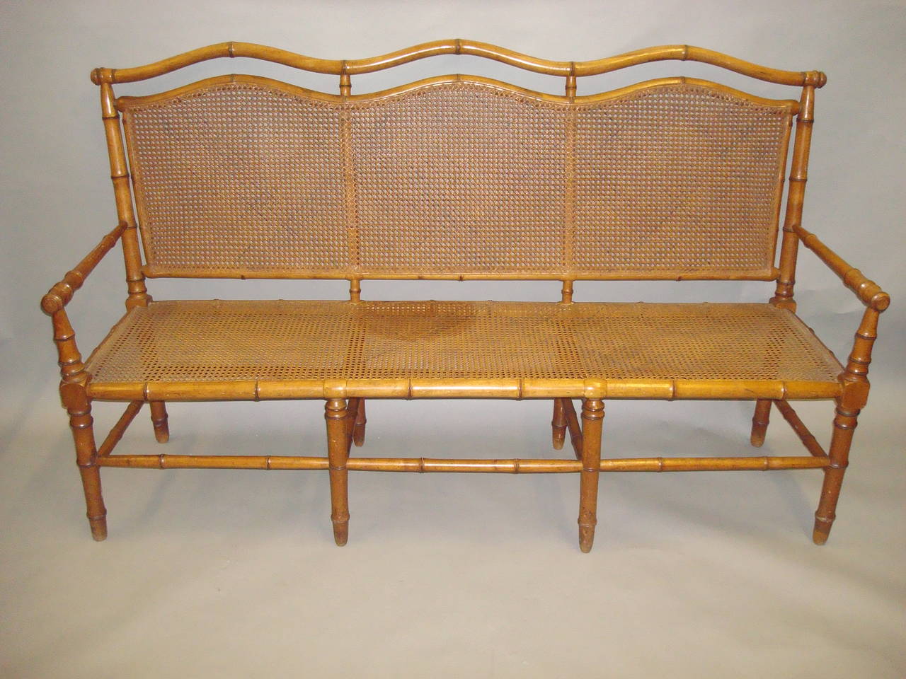 A stylish 19th century cherrywood faux bamboo settee or hall seat; the shaped back incorporating three cane panels within a faux bamboo frame leading to tapering straight arms, above a cane seat, all raised on faux bamboo legs joined by similar