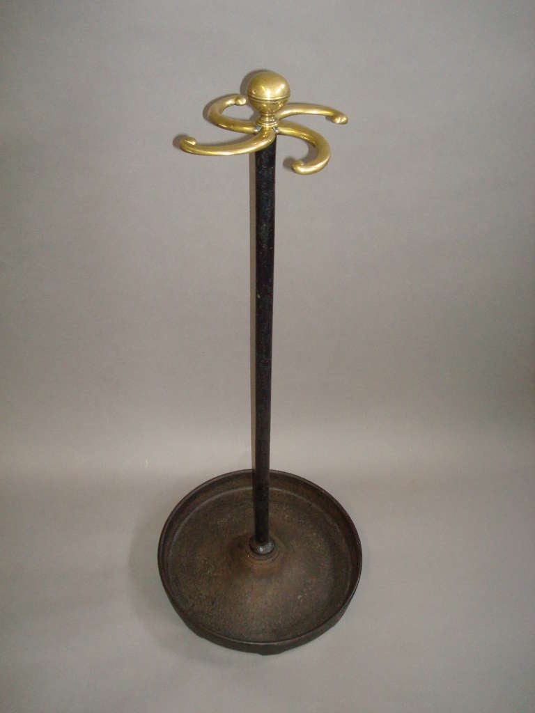 An unusual Regency cast iron and brass stick stand of tall proportions; the central brass knob handle with four scrolled arms, raised on an iron column, on a heavy circular dished base.