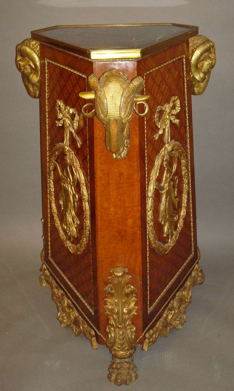 A flamboyant Louis XV style ormolu mounted, walnut and kingwood pedestal, the triangular 'St Annes' marble top with a gilt brass moulded edge raised on a tapering triangular pedestal, headed with large ormolu rams head mounts to the canted corners;