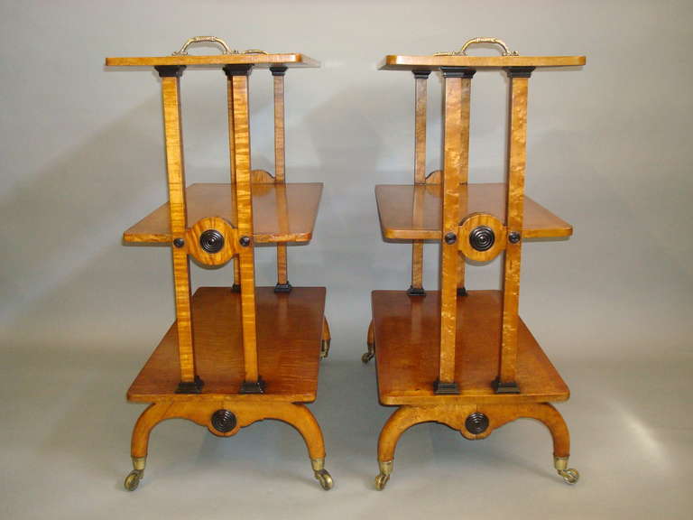 A splendid Regency matched pair of maple etageres; the rectangular top of the three graduating tiers with ebony stringing and ornate brass carrying handles to either side, raised on twin end supports inlaid with ebony banding and ebonized mouldings,