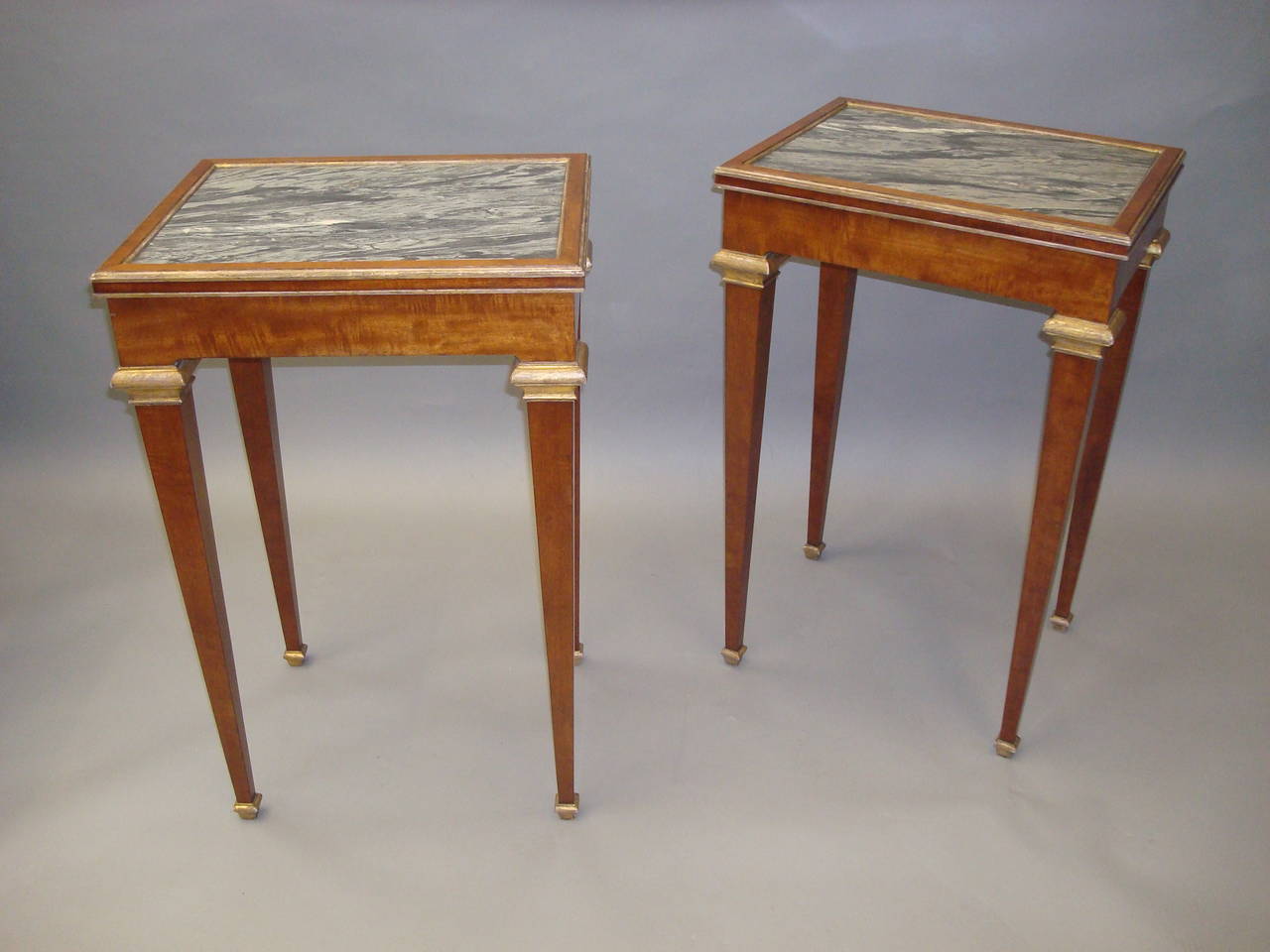 A stylish 19th century pair of mahogany, marble top, end tables; the grey 'Bleu Tigre' rectangular marble tops inset in a fiddleback mahogany crossbanded frame, with narrow giltwood mouldings; the simple frieze also in fiddleback mahogany raised on