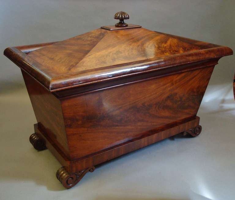 An impressive Regency flame mahogany cellarette of large proportions; the well figured rectangular hinged lid surmounted by a large reeded finial, revealing a fitted, lift out, interior with apertures for bottles; the lid set within a bold curved