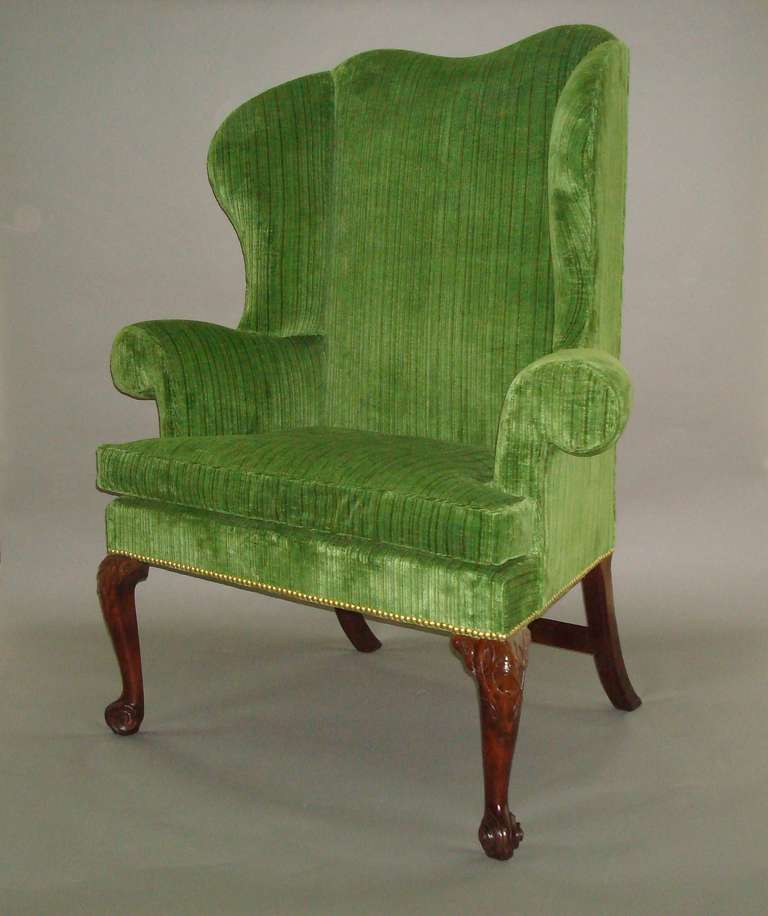 An impressive George II mahogany wing chair or porters chair of fabulous shape and unusual wide and shallow proportions, the padded back with a dipped centre leading to the flared wings above exaggerated scrolled arms, the high shallow seat with a