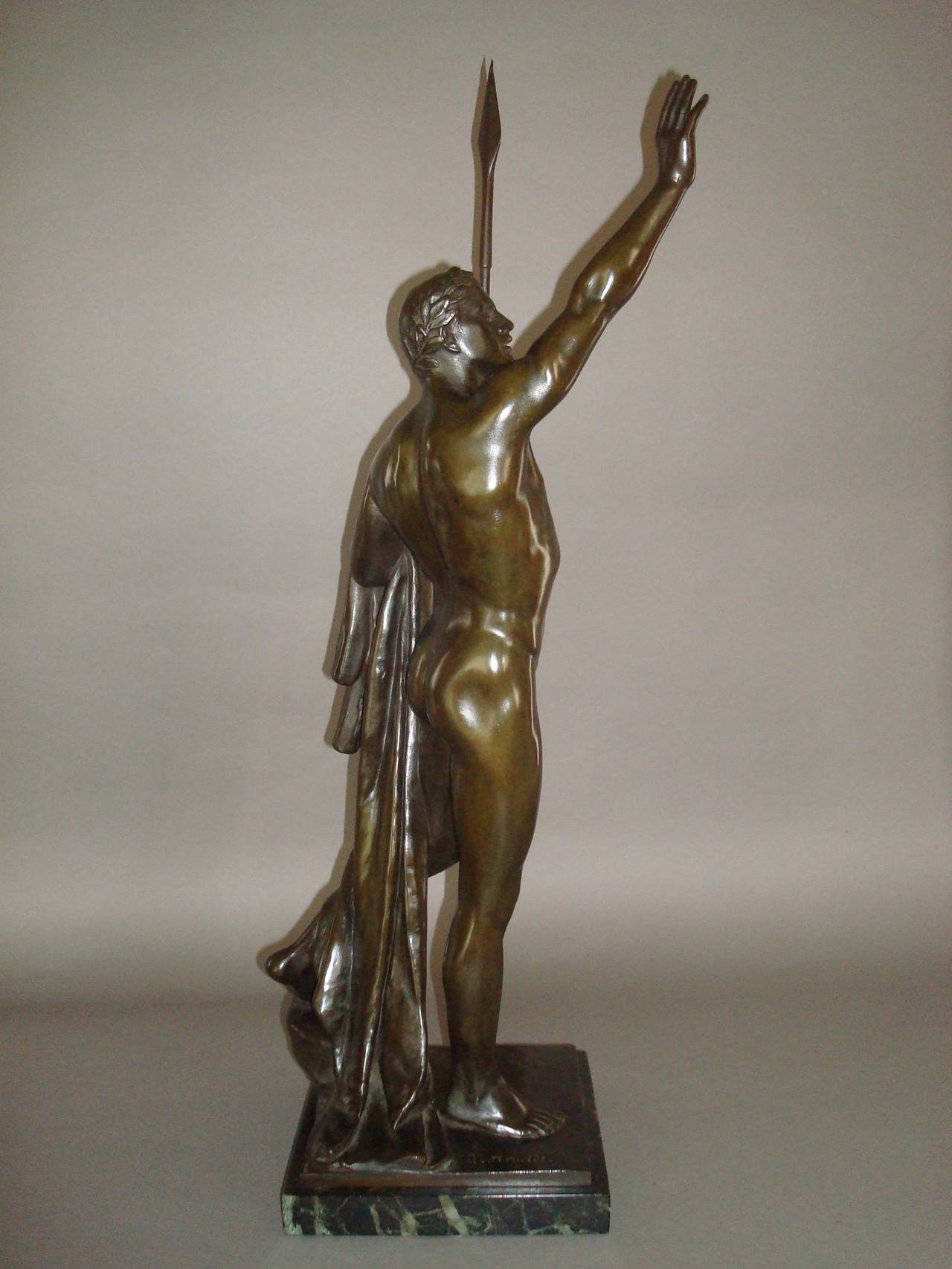 A 19th century bronze sculpture of a victorious nude athlete,  with his right arm raised triumphantly, his left hand holding a javelin and a robe draped over his arm; with a rich brown patina, raised on a verde antique marble plinth.  
Signed 'H