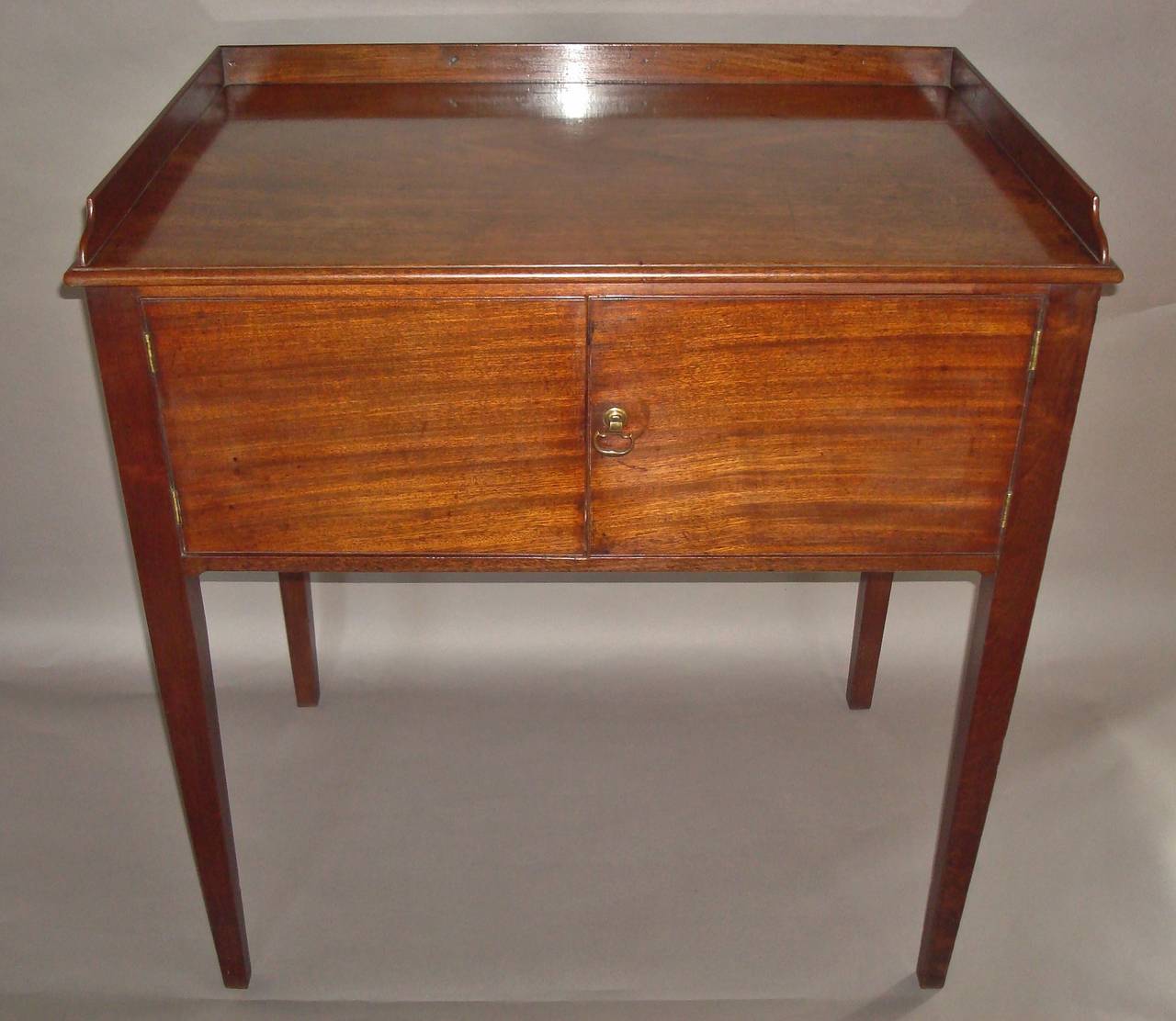 George III mahogany bedside table in Chippendale style,  of unusually large proportions; the very well figured rectangular top with a thin moulded edge and a three quarter gallery above a pair of cupboard doors with brass axe head handle with a