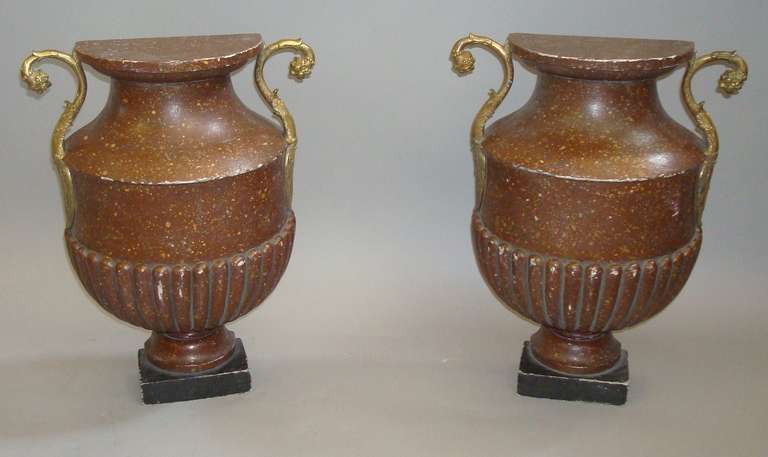 A 19th century unusual pair of faux porphyry flat back urns, the campana shaped body with demilune flat top and a carved gadrooned base painted to simulate porphyry standing on a black plinth; with gilt bronze scrolled mounts with acanthus