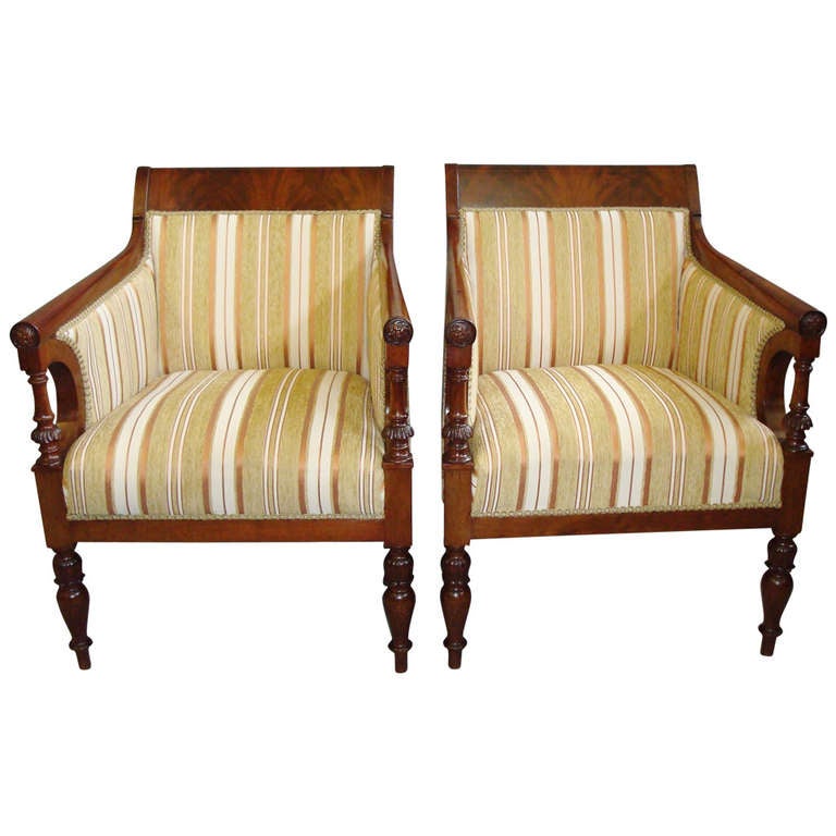An elegant C19th pair of French mahogany armchairs; the curved crest rail in book matched flame mahogany above a padded rectangular back, the arms of gun barrel form terminating in carved roundels above curved arm supports fronted by turned acanthus