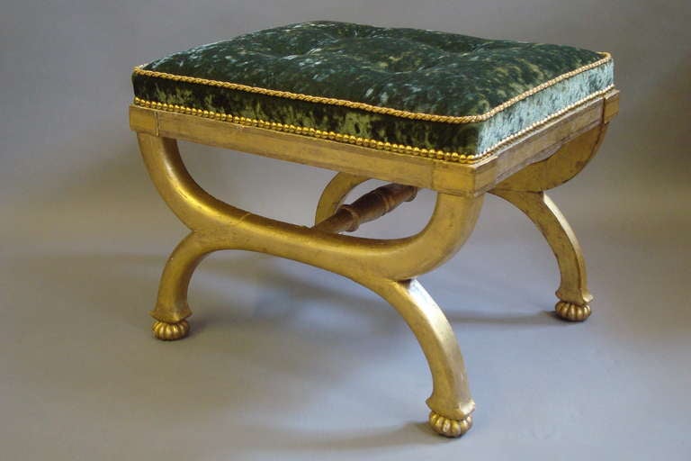 A good Regency giltwood X-frame stool; with lovely original water gilding. The X-shaped supports on fluted bun feet, with a central turned stretcher. Newly upholstered in buttoned green velvet.