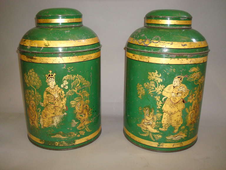 A good pair of English 19th century japanned tole tea canisters of typical cylindrical form, with lovely original green and gilt decoration. The domed tops retaining their original lids, and the fronts each with a different Chinese scene of figures