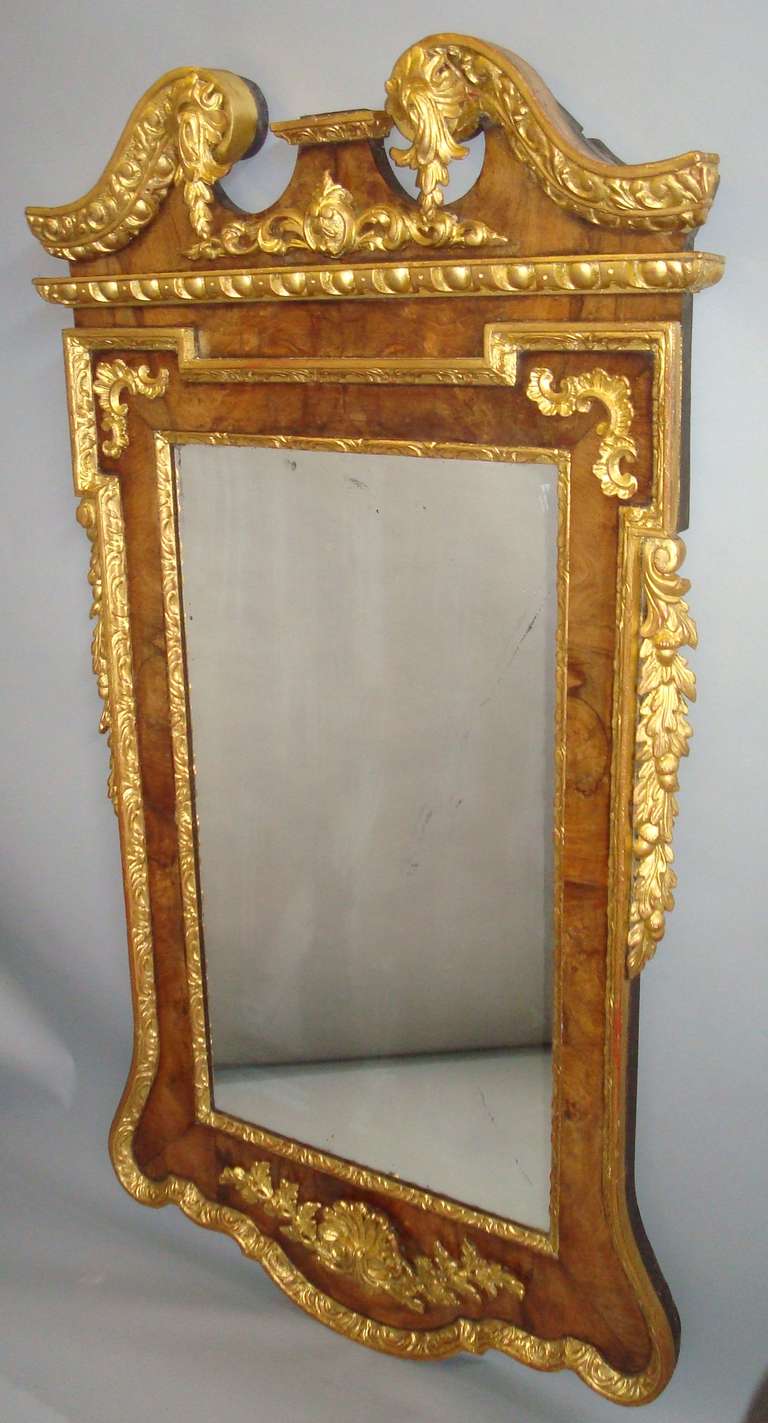 An impressive George II walnut and parcel-gilt wall mirror, the swan neck pediment with scrolled egg and dart carving terminating in carved flower heads centred with trailing leaves; the rectangular mirror plate within a carved slip and a moulded