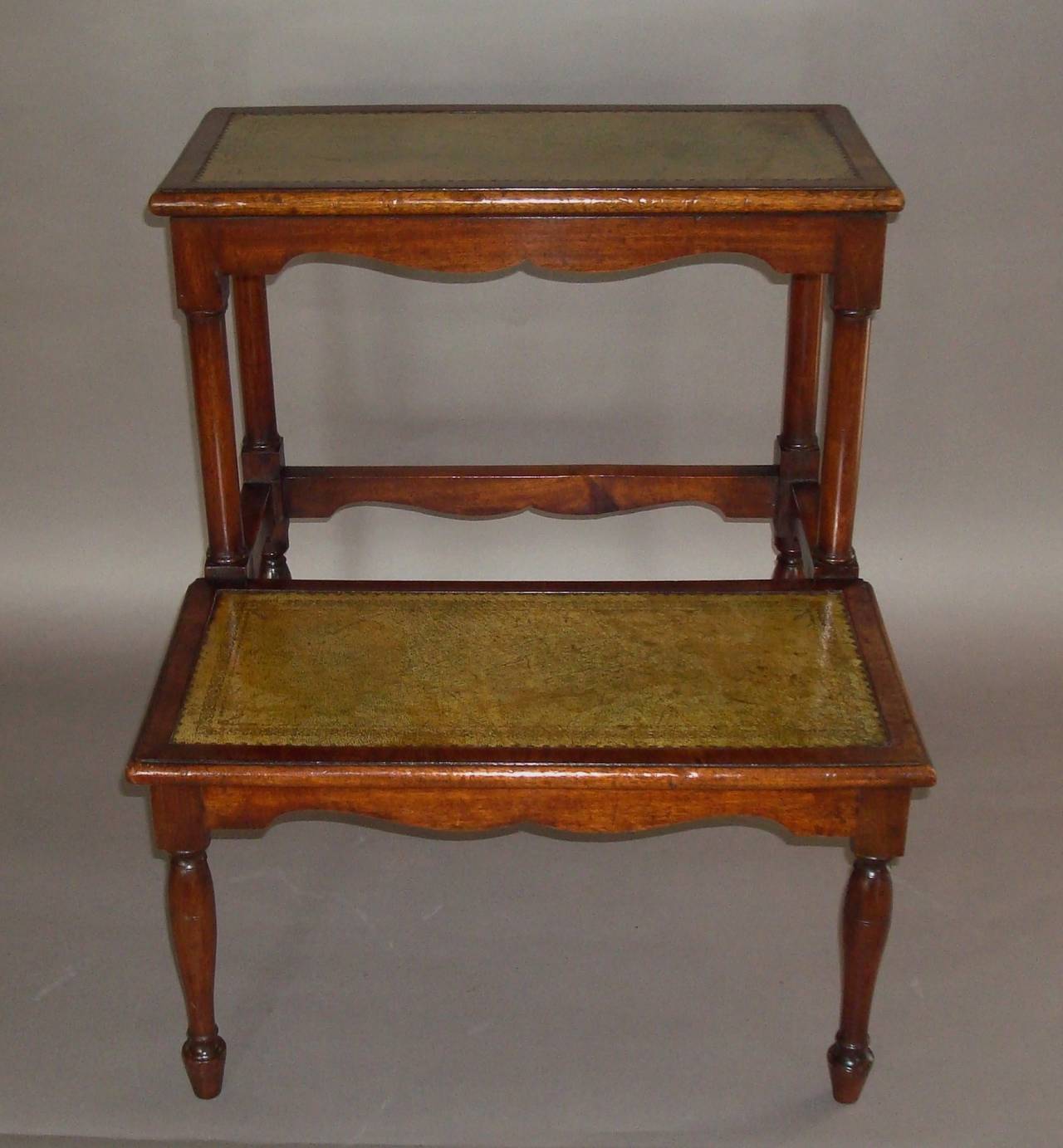 A good Regency set of mahogany library steps of elegant proportions, the two treads with a moulded edge and narrow mahogany cross banding inset with olive green leather with gilt tooled borders.  The top tread supported on turned columns and shaped