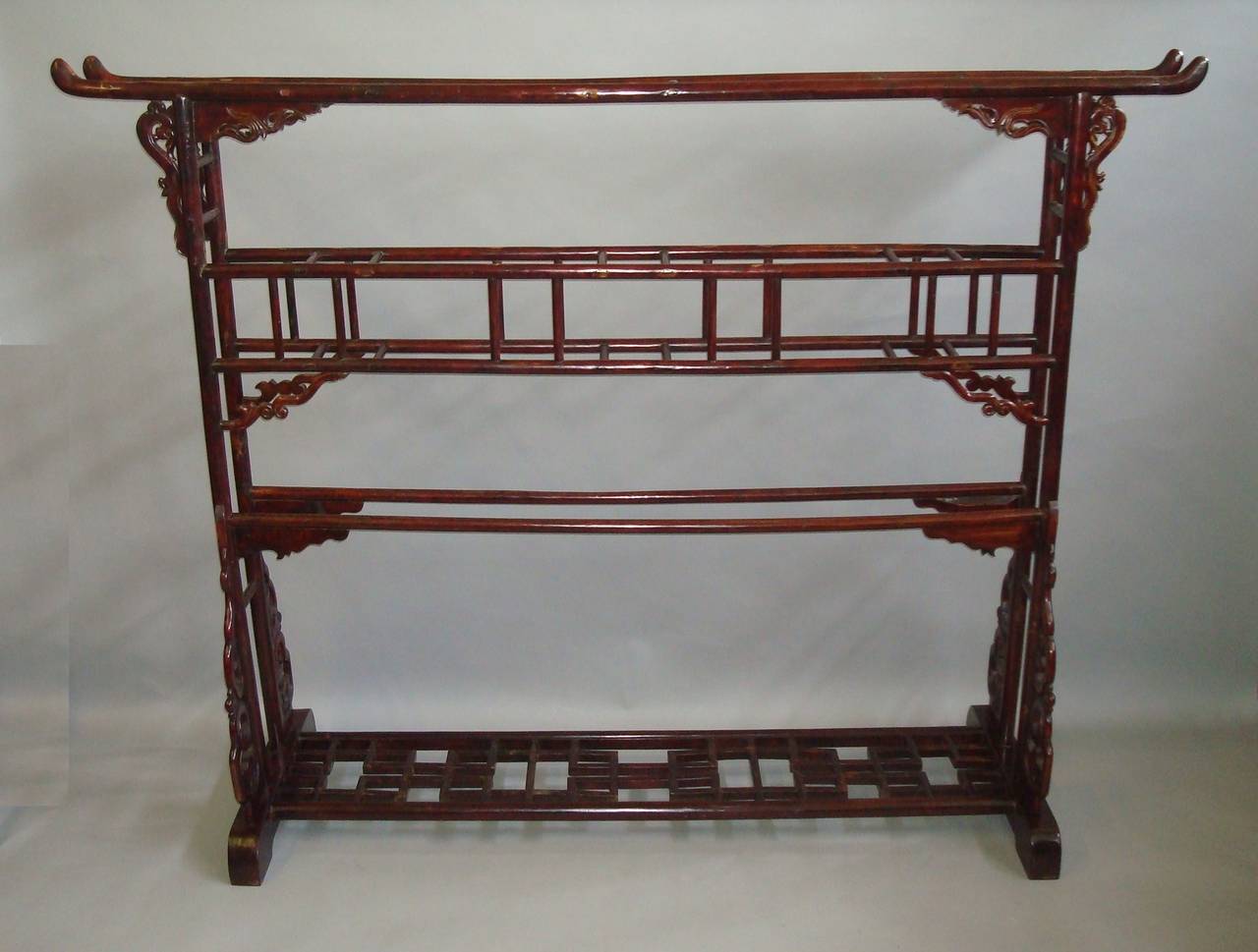 An interesting 19th century Chinese lacquered robe stand/clothes horse of large proportions, the twin top rail with raised ends, on turned end supports, the central rails terminating in scrolled brackets and the wide base stretcher of a pierced