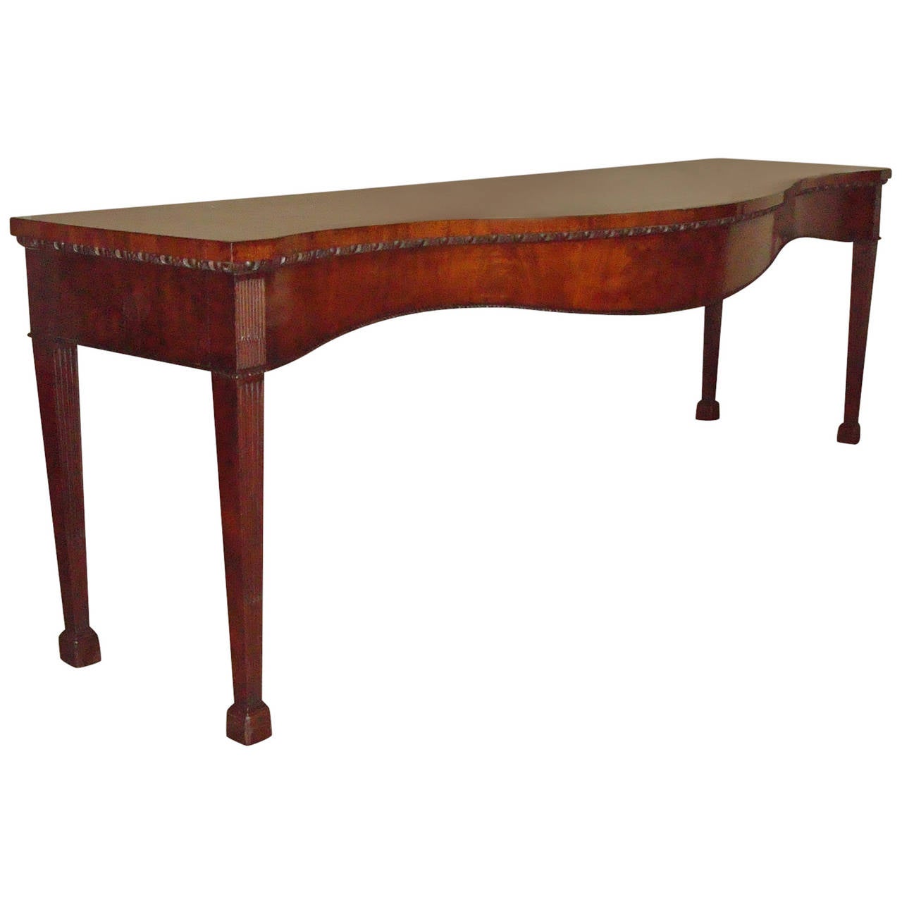 An exceptional George III mahogany, serpentine serving/side table of monumental proportions; the figured mahogany top with an exaggerated serpentine front, but the whole still retaining desirable shallow form, with a finely carved egg and dart