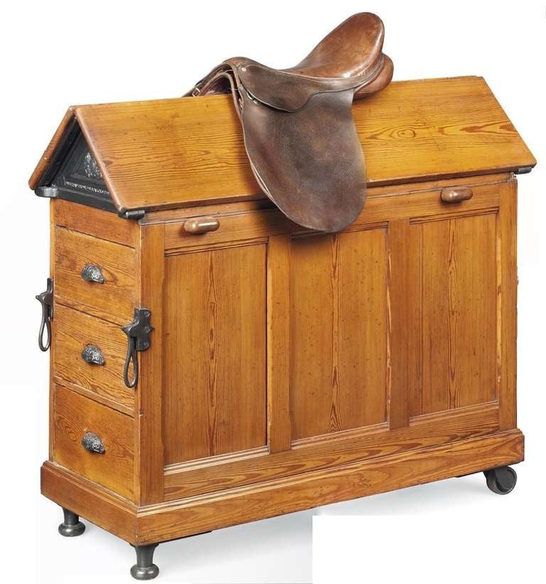 Late C19th Pitch Pine Saddle Horse, by Musgrave & Co Ltd, with an angled and hinged top and two removable iron poles joined by a brass pole, one short side with three drawers, the other with a cupboard enclosing a shelf, on castors, with cast iron
