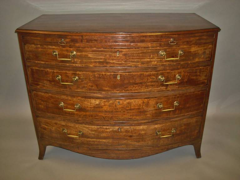 A fine George III mahogany bow front chest of drawers, the well figured mahogany top with boxwood stringing and a crossbanded border and a slender moulded edge above a brushing slide with a baize lining and brass axe head handles.  The four long