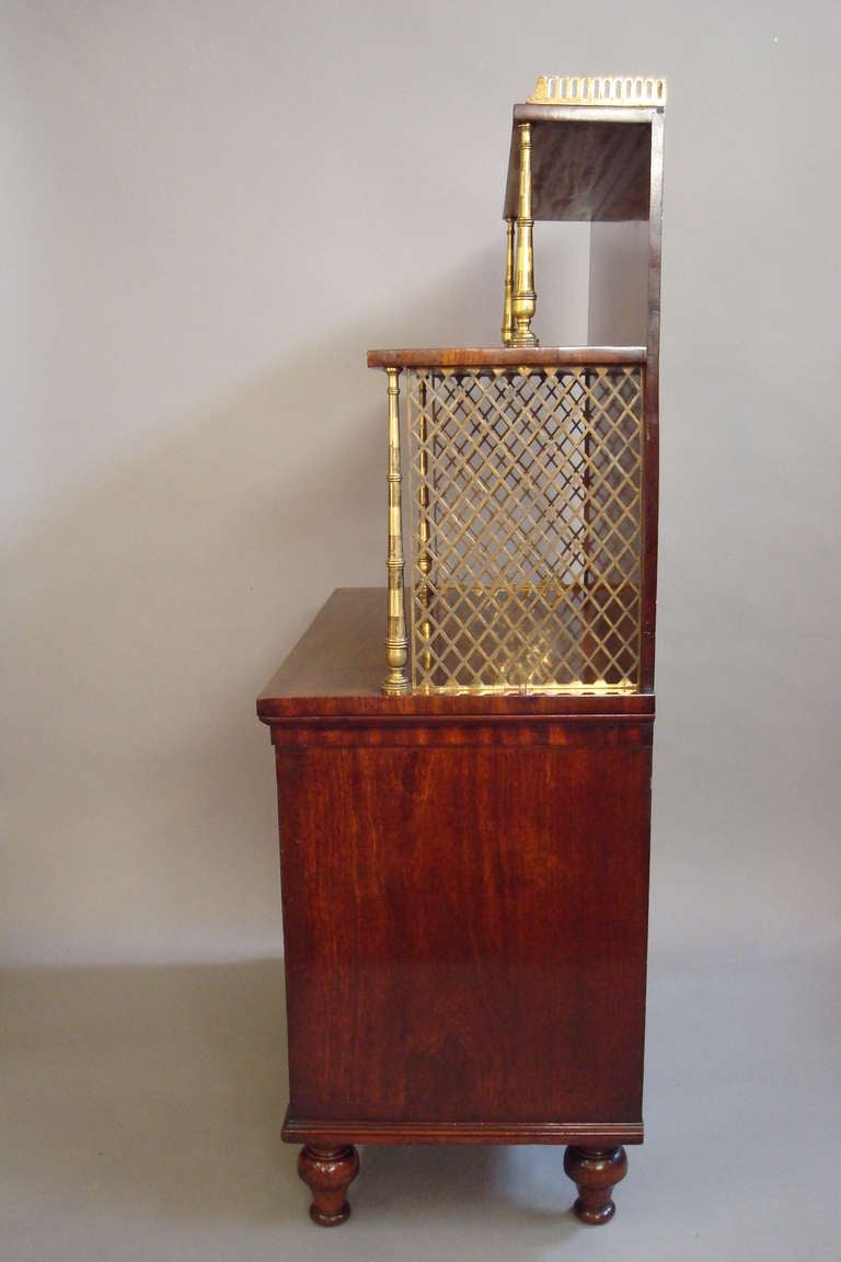 Regency mahogany side cabinet or dwarf bookcase of small proportions. The shelf back with gilt brass gallery and gilt brass baluster supports with pierced trellis grills to either side, above a pair of well figured panelled doors raised on turned