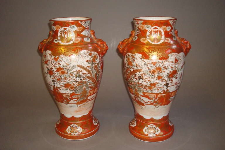 A late 19th century pair Japanese kutani vases, decorated in coral, gilt and green on a white background. Each depicting scenes of ladies picking flowers the reverse with peacocks and foliage.  Each side mounted with the head of a mythical creature.