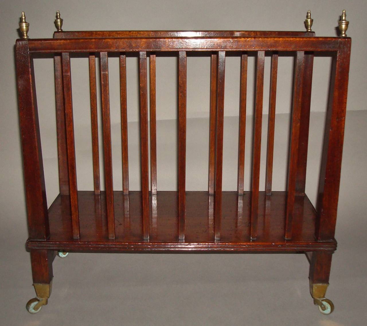 An unusual Regency mahogany canterbury / folio stand of elegant proportions, the square tapering end supports terminating in brass finials united by a moulded top rail incorporating seven square slats to either side, raised on a platform base with a