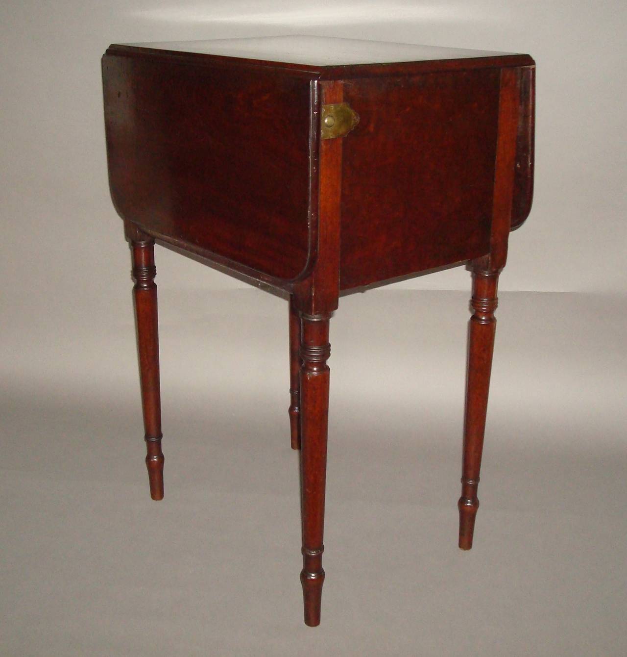 A rare Regency mahogany deception table, the rectangular top with a moulded edge and a conventional drop leaf to the one side, and a fall front to the other side disguised as a drop leaf, released with brass release buttons to either side and brass