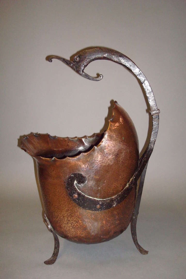 An unusual Late C19th Arts and Crafts iron and copper 'nautical' coal scuttle; the iron handle in the form of a fishes head sweeping down to a scroll, supporting the beaten copper body in the form of a shell, with scalloped edge supported on swept