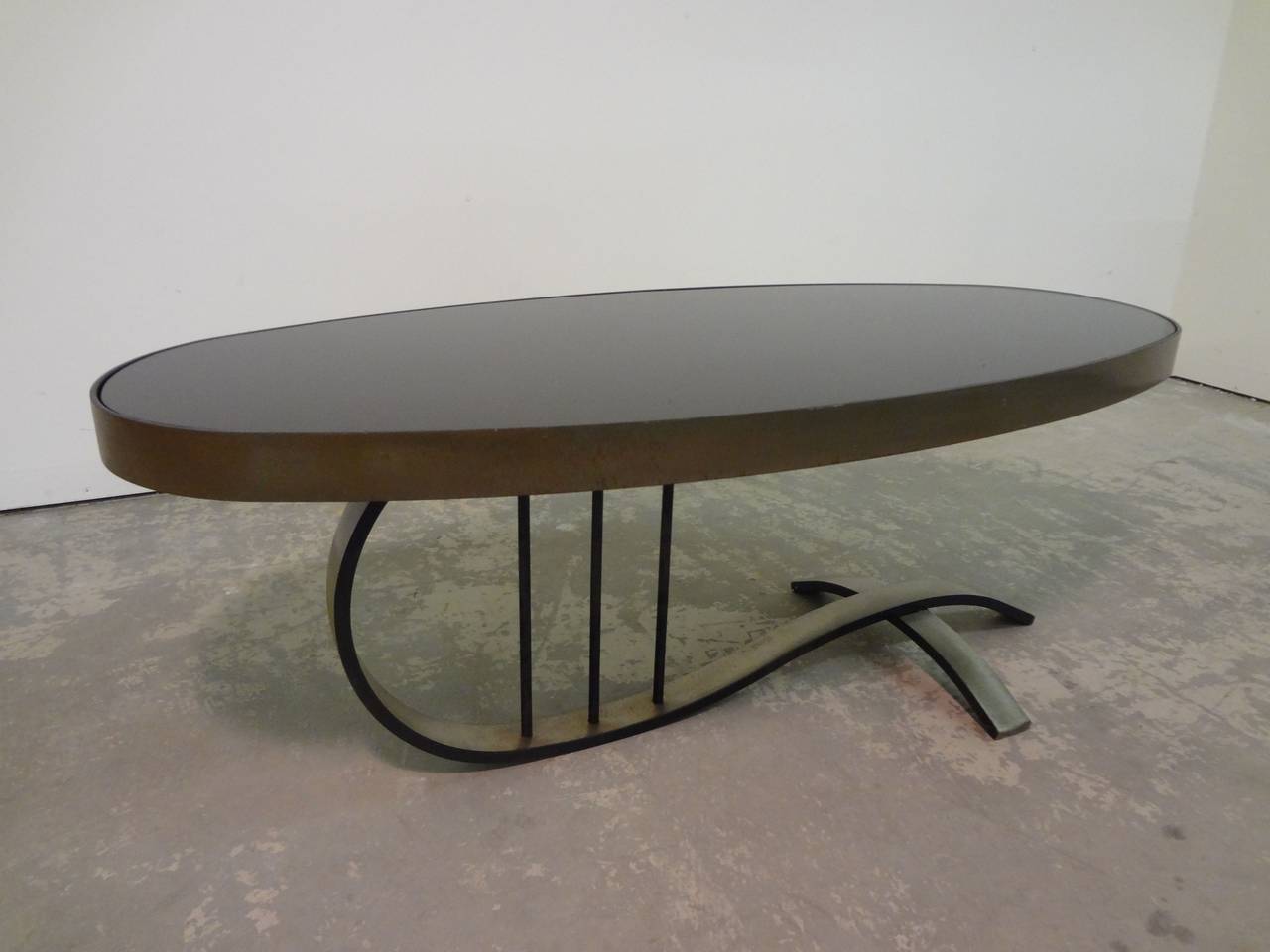 Sophisticated French cantilevered cocktail table, circa 1960s. Very heavy metal frame, looks to be solid steel with some sort of patinated bronze finish. Black under painted glass top in excellent condition and patina to the table base as expected