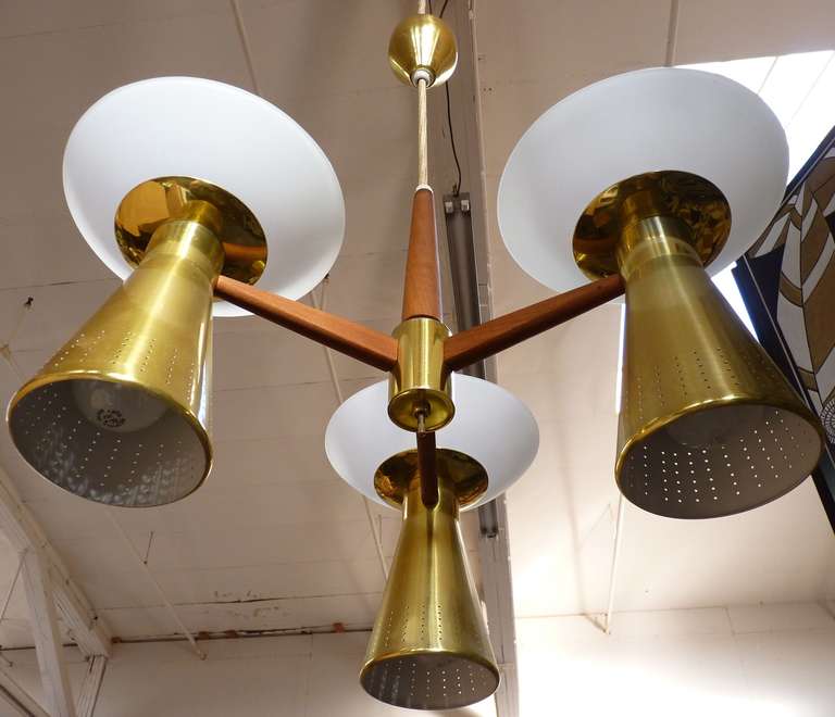 Believed to be designed by Paavo Tynell, this pair of Adjustable Height, 3-arm Chandeliers for Lightolier c.1950's sports perforated brass cones that reflect light below and matte opaline concave diffusers act as torchieres and add more ambient