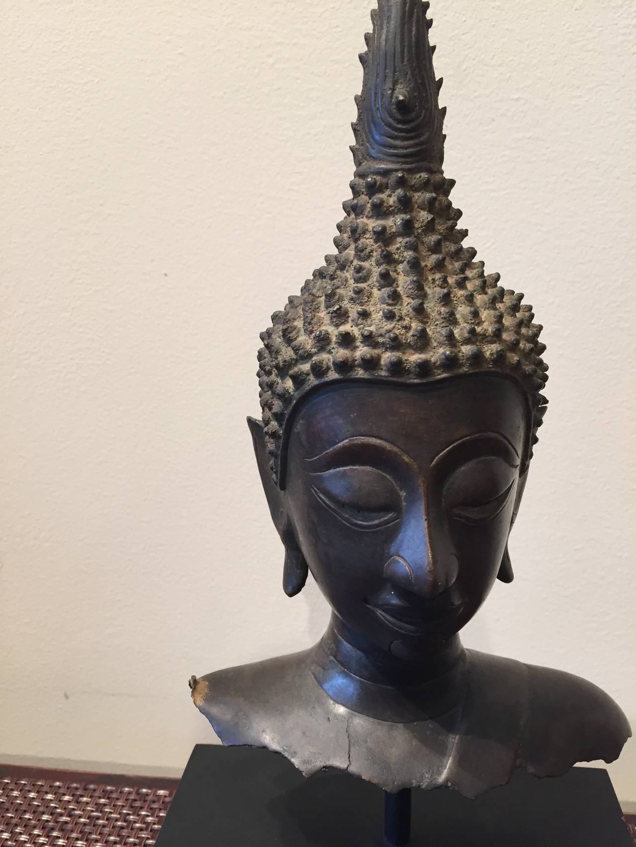 A striking, small Thai bronze Buddha bust floating over a simple black base. Thailand, c. 1920.
Measurements:  
Buddha : L: 6.5  D: 2.5 H: 10 
With Stand: L: 6.5  D: 3.5  H:13
BH2010