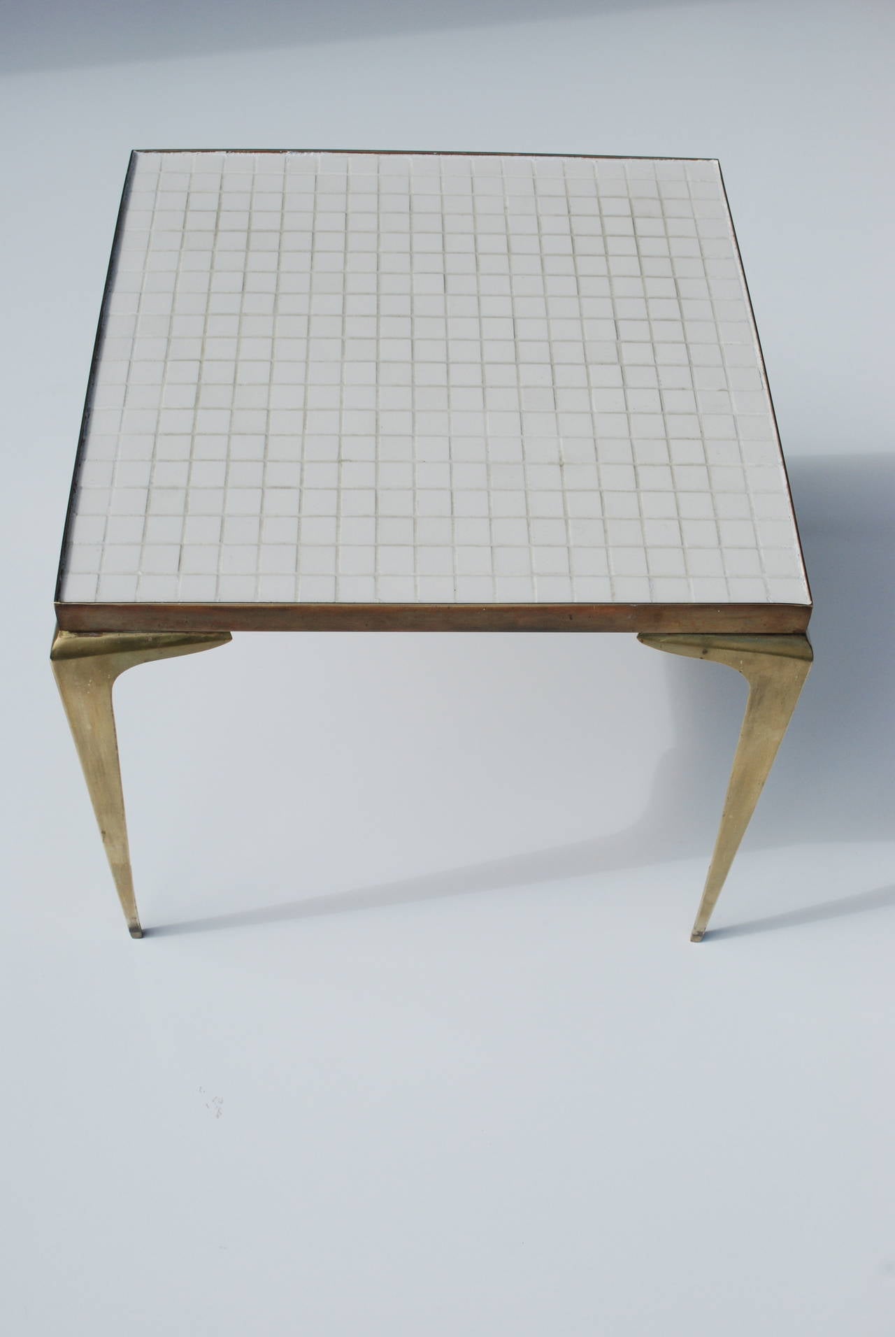 This is a beautiful table with pointed brass legs that are stamped made in Japan. The table is made of white glass mosaic tiles. 
We have a coordinating coffee table in a separate posting.