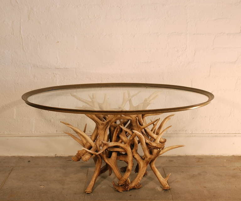 This artfully assembled arrangement of antlers makes a striking 
base for this coffee table.  It has an organic sculptural quality to it.
The top is a large oval shaped glass tray trimmed with brass.