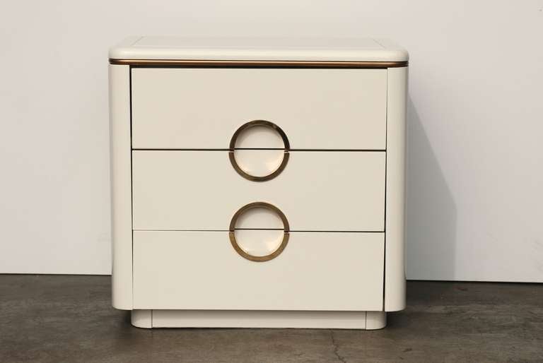 A two drawer vintage nightstand manufactured by Mount Airy Furniture Co.
It has been finished in a bone off white color to offset the original brass handles which have a Gucci-esque style. 
We have a matching six drawer dresser in a separate