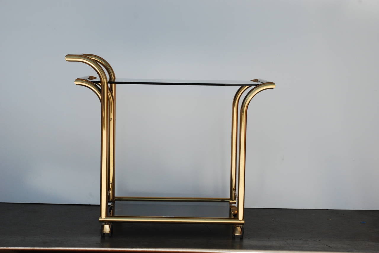 A sleek two-tiered Italian vintage bar cart with new tempered smoked glass. The brass is in very good vintage condition. The cart retains the 'made in Italy' sticker. The measurement to the top-tier is 26