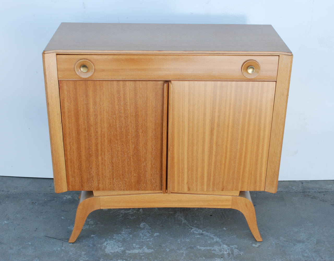 This sweet little cabinet attributed to Gilbert Rohde (1894-1944) would make a great dry bar. It is made of blonde mahogany. The top drawer face hinges open flat. The double bottom doors have integrated handles and open to reveal an interior shelf.