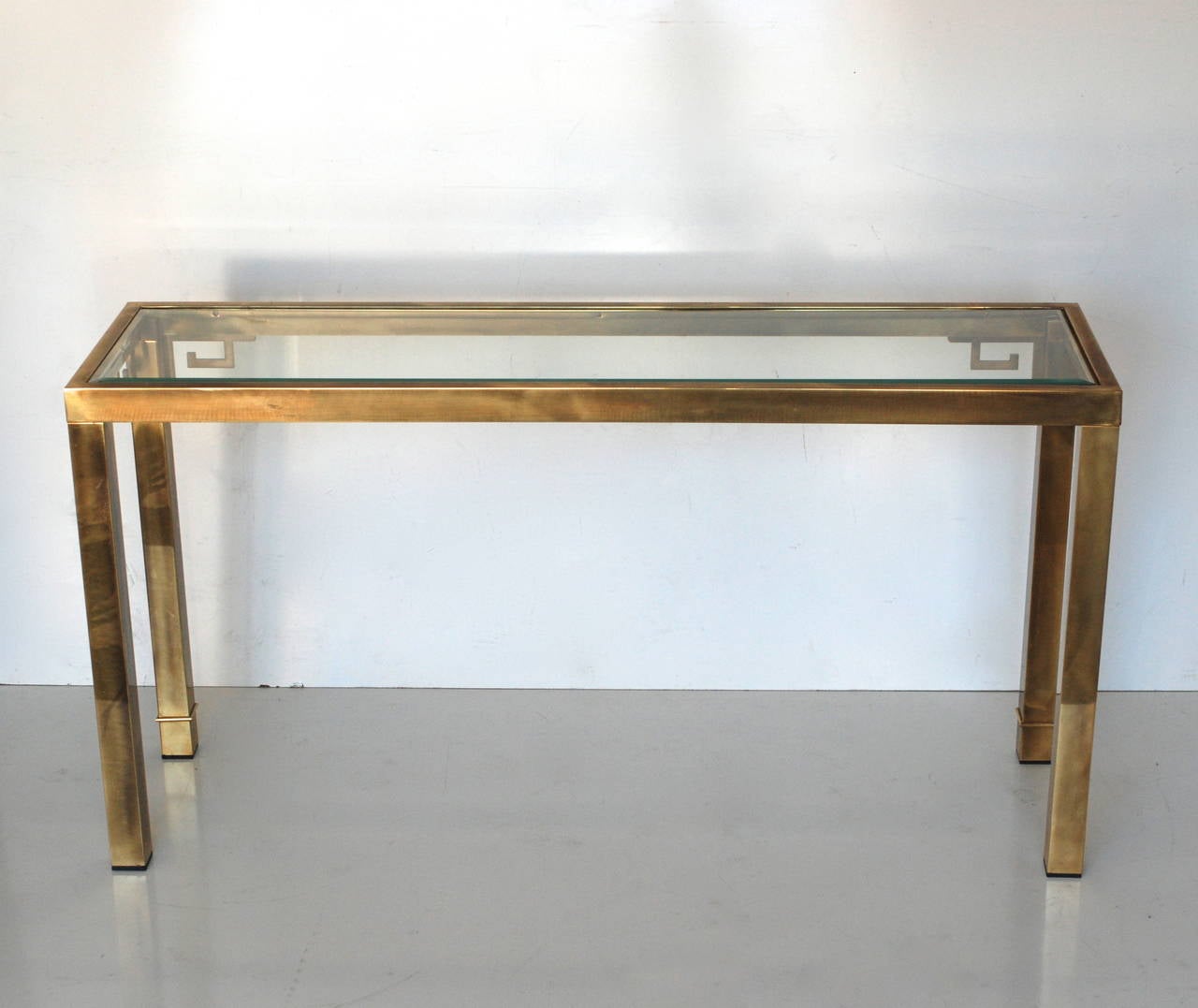 A solid brass console manufactured by Mastercraft. There is a beveled glass top that sits flush on the top of the piece. The brass has a nice warm antique patina to it.